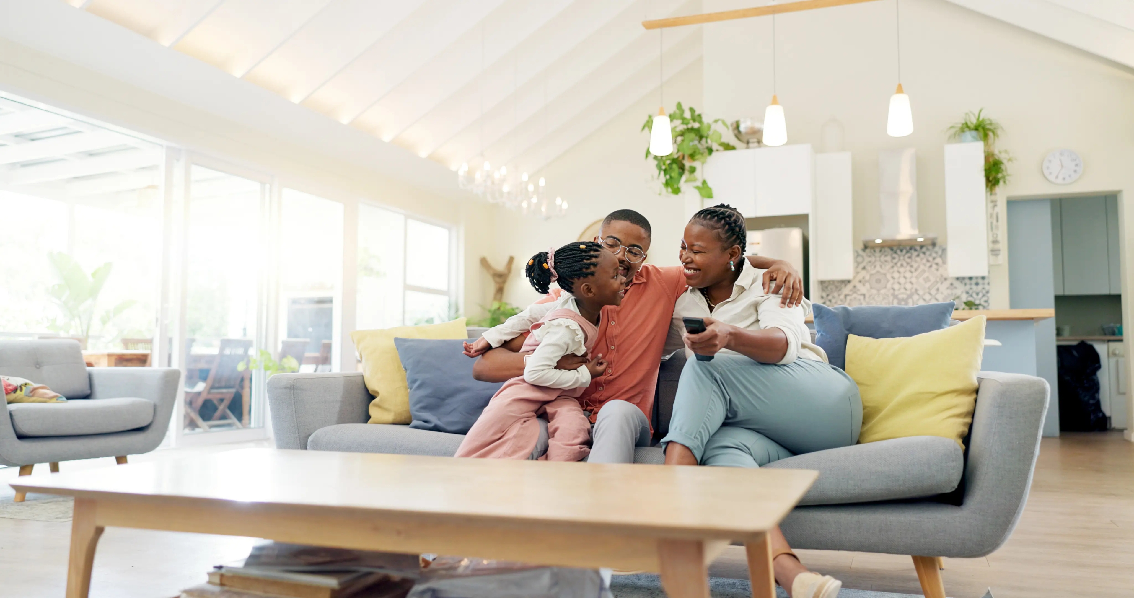 Family of three relaxing and smiling together on a cozy sofa in a bright, modern living room.